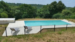 Una piscina rectangular con solárium empedrado, rodeada por una cerca de metal.