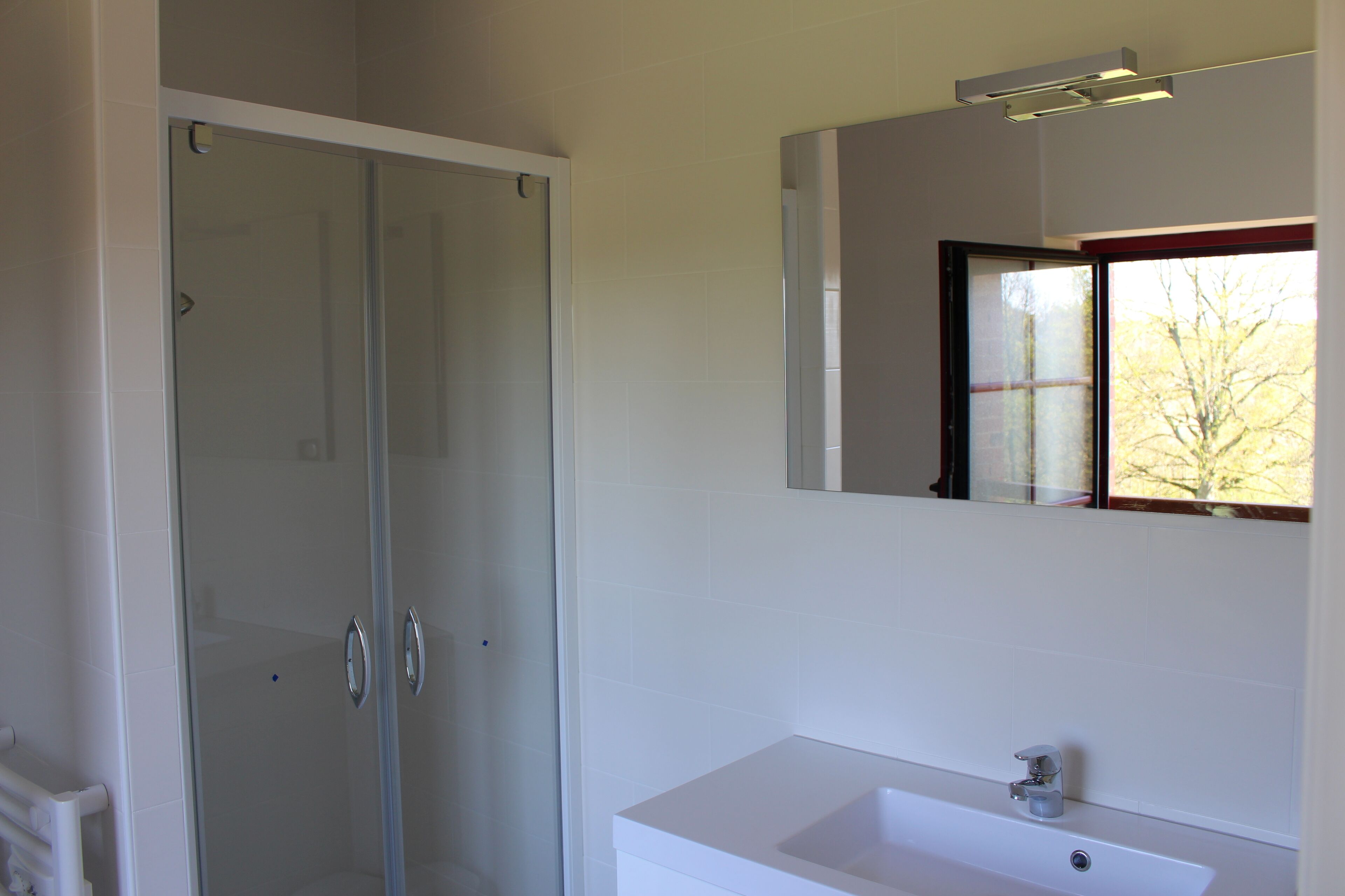 Een badkamer met een douchecabine met glazen deur, een witte wastafel en een spiegel boven de wastafel.