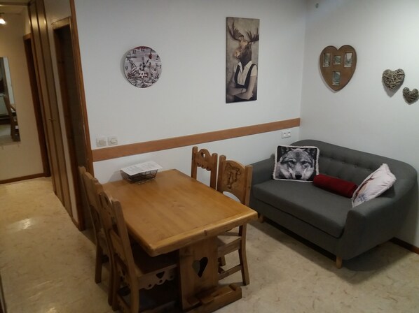 A dining area with a wooden table and chairs, a grey sofa with a wolf-themed pillow, and wall art including a deer and a heart-shaped decoration. - Self-contained apartment in house in Cauterets  (Hautes-Pyrénées)