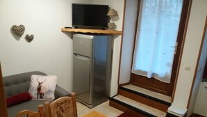 A compact living space with a kitchenette, a dining table, a sofa with a decorative pillow, and a window with a curtain. - Self-contained apartment in house in Cauterets  (Hautes-Pyrénées)