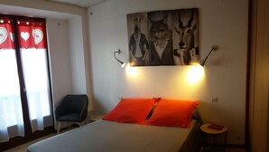A bedroom with a bed, two red pillows, a chair, a small round table, and wall art. - Self-contained apartment in house in Cauterets  (Hautes-Pyrénées)
