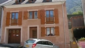 A two-story building with wooden shutters, a car parked in front, and a sign indicating it is an apartment building. - Self-contained apartment in house in Cauterets  (Hautes-Pyrénées)