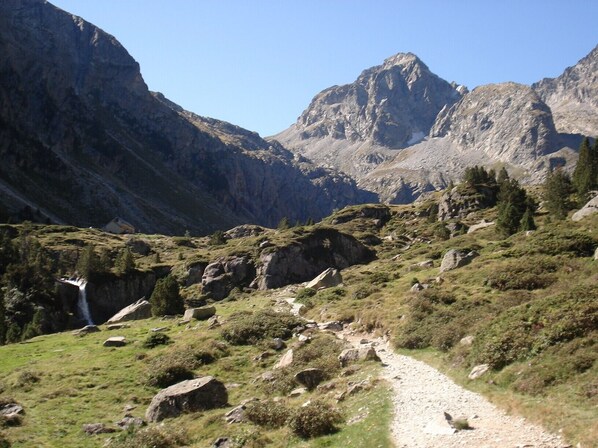 A mountainous landscape with a dirt path leading through rocky terrain and sparse vegetation.
