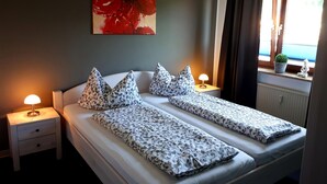 A double bed with patterned bedding, two bedside tables with lamps, a wall-mounted painting, and a window with a view. - Modern apartment in the heart of Schleswig (Schleswig)