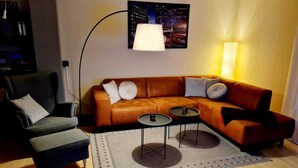 A modern living room with a leather sofa, two side tables, a chair, and a cityscape painting on the wall. - Modern apartment in the heart of Schleswig (Schleswig)
