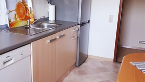 A modern kitchen with a Bosch dishwasher, a stainless steel refrigerator, and a sink with a faucet. There is a clock on the wall and a door to the right. - Modern apartment in the heart of Schleswig (Schleswig)