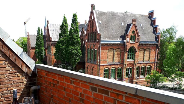 A rooftop terrace with a brick wall, a table with a bottle and glass, and a patterned cushion. - Modern apartment in the heart of Schleswig (Schleswig)