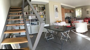A modern kitchen with wooden cabinets, a dining area with a table and chairs, and a staircase with bookshelves. - traditional stone village house (Olmeta-Di-Tuda)