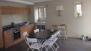 A modern kitchen with wooden cabinets, a gas stove, an oven, a sink, and a dining area with a table and chairs. - traditional stone village house (Olmeta-Di-Tuda)