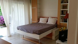 Une chambre à coucher moderne avec un lit, une table de chevet, une bibliothèque et une fenêtre avec des rideaux.