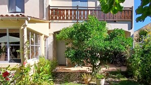 A two-story house with a balcony, a covered patio, and a garden with potted plants.
