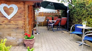 An outdoor patio with wooden walls, a heart-shaped decoration, a hanging planter with flowers, and outdoor furniture.