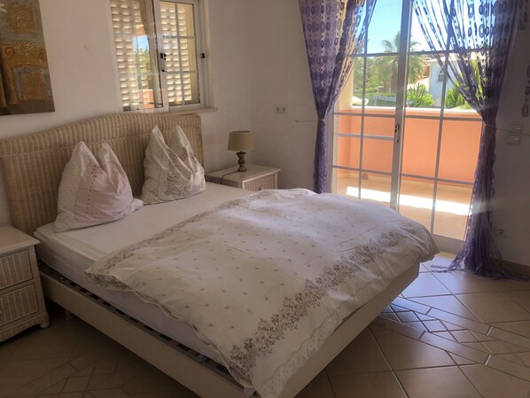 A bedroom with a bed, nightstands, a lamp, and a view of the outdoors through a window with curtains.