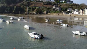 Een kustgebied met boten in kalm water, een zandstrand en huizen op een heuvel.