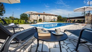 A poolside area with lounge chairs, a table with a book and a cup, and a pool. - Stylish Istrian Retreat with Pool, Tennis Court & Outdoor Kitchen (Pican)