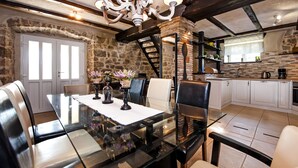 A dining area with a glass table, black chairs, and a chandelier. There is a stone wall and a kitchen in the background. - Stylish Istrian Retreat with Pool, Tennis Court & Outdoor Kitchen (Pican)