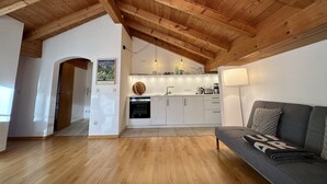 A spacious living area with a wooden ceiling, a kitchen with white cabinets, and a grey sofa with a blanket.