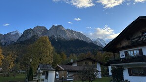 A mountain landscape with a chalet-style building in the foreground, featuring a balcony and a traditional design.