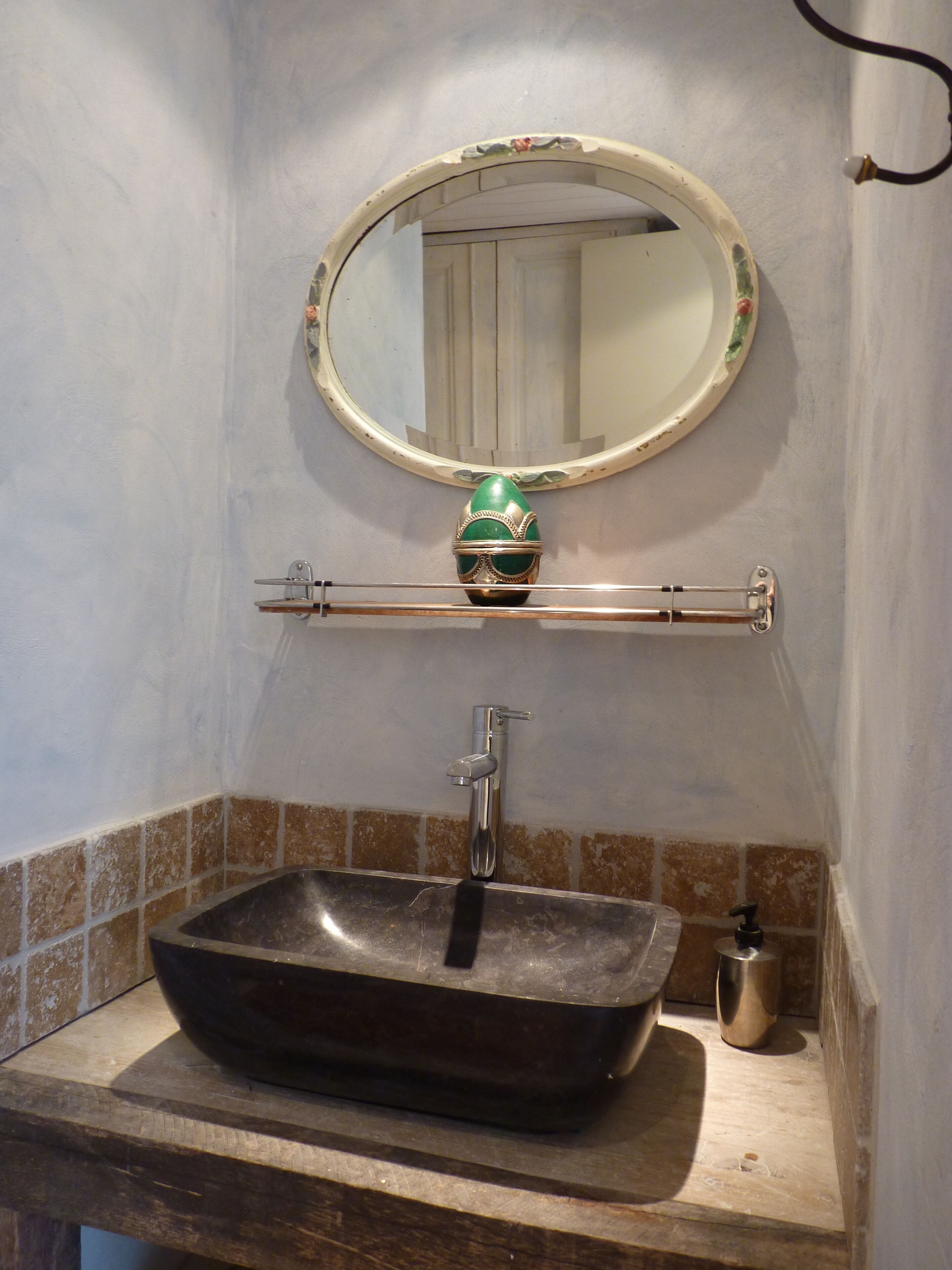 Un baño con un lavamanos rectangular, un espejo con marco decorativo y un estante pequeño con un objeto verde.