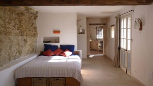 Ein Schlafzimmer mit Bett, Kissen, einem hölzernen Kopfteil, einem Fenster und einer Tür, die auf einen Balkon führt.