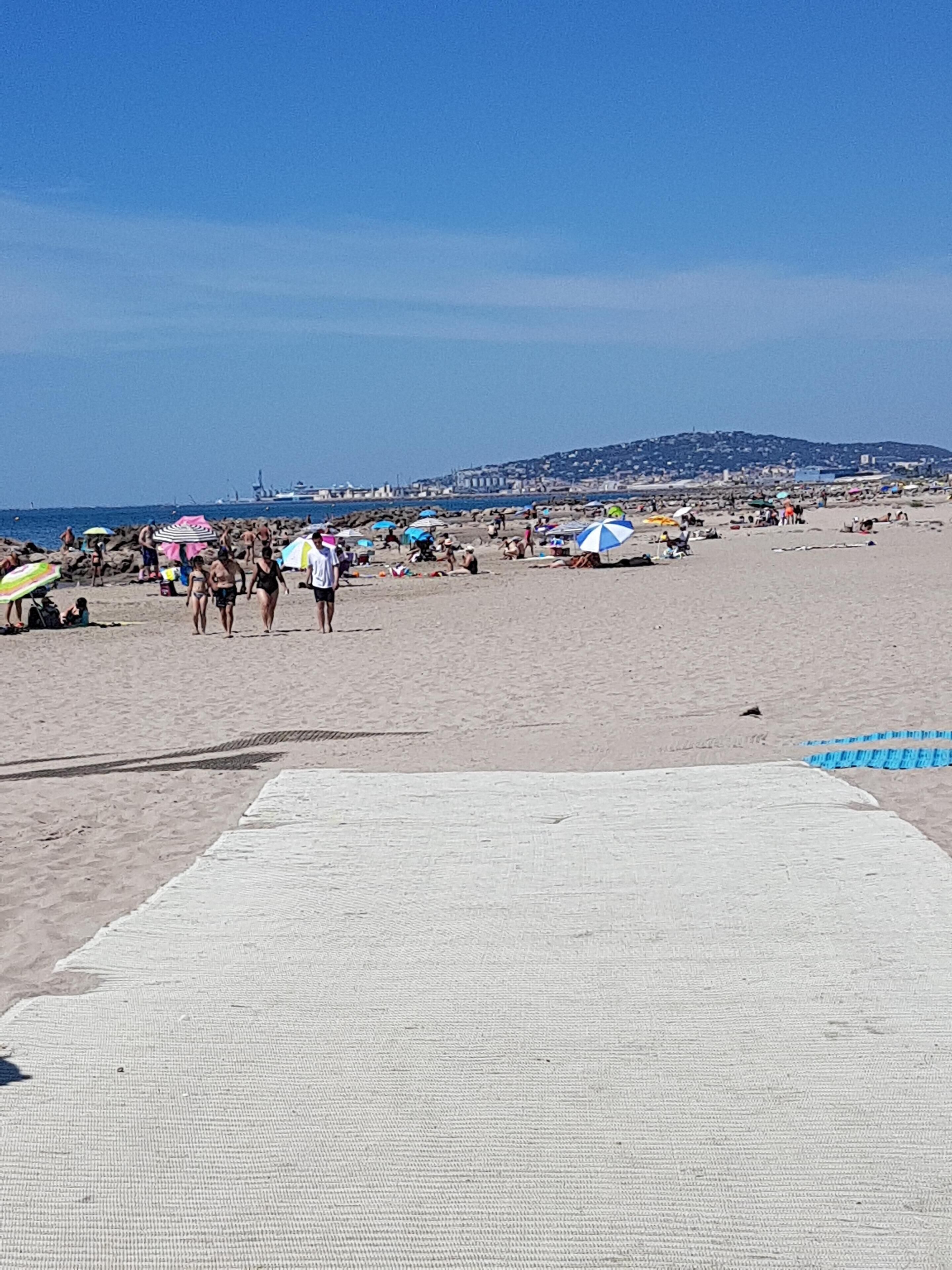 Platja amb gent, ombrelles i un paisatge urbà a la distància.
