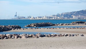 A coastal cityscape with industrial buildings and a rocky shoreline.