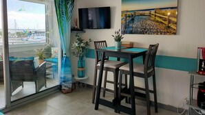 A dining area with a table and chairs, a TV mounted on the wall, and a view of the marina through a glass door.