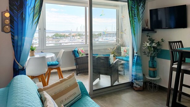 A modern living room with a large sliding glass door, a flat-screen TV mounted on the wall, and a view of a marina with boats.