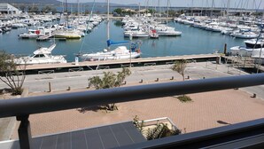 A marina with numerous boats docked, a clear sky, and a hilly landscape in the background.