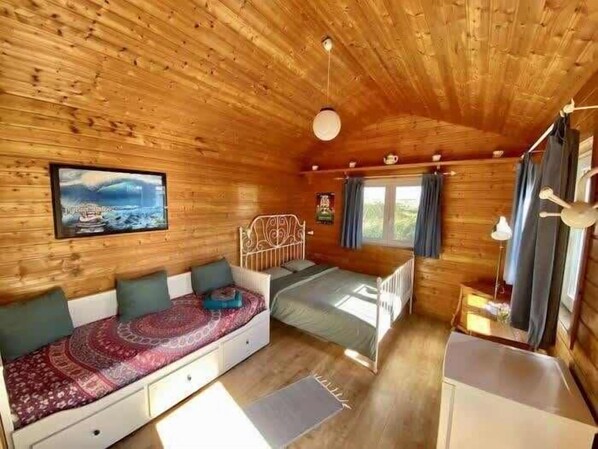 Un acogedor interior de cabaña con cama, sofá, mesa de comedor y ventana con cortinas.