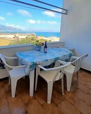 A balcony with a table and chairs, a bottle, and a view of the sea and landscape.