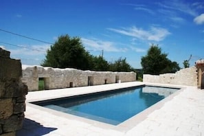 Une piscine rectangulaire avec des murs en pierre et une terrasse carrelée.