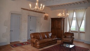 Una sala de estar con un sofá de cuero marrón, un sillón de cuero, un aparador de madera y una araña.