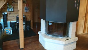 Une pièce chaleureuse avec une cheminée, des étagères en bois remplies de livres et d’objets décoratifs, et un escalier.