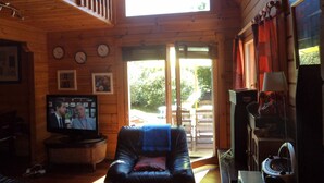 L’intérieur chaleureux d’un chalet avec un canapé en cuir, un téléviseur, des murs en bois et une grande fenêtre.