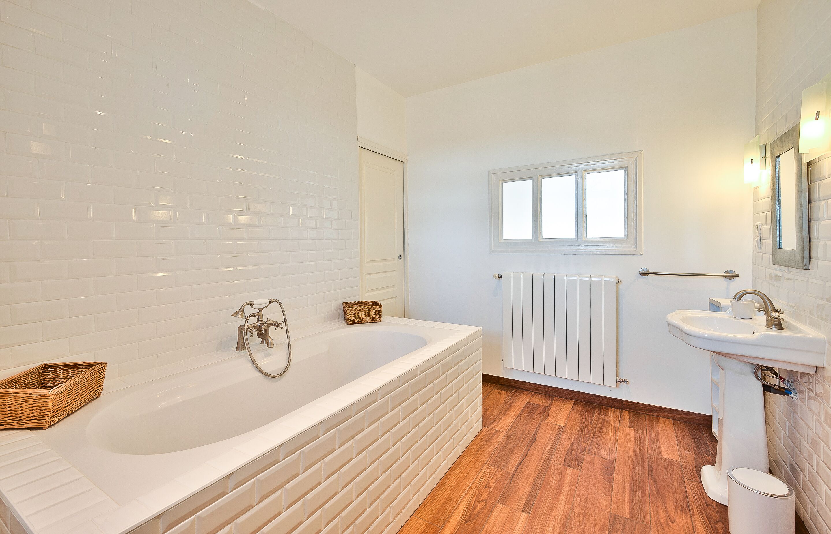 A modern bathroom with a large bathtub, a white sink, and a wooden floor.