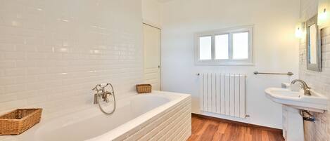 A modern bathroom with a large bathtub, a white sink, and a wooden floor.