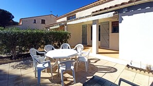 A patio with a round table and white chairs, a small black bench, and a white building with a tiled roof. - semi-detached villa sleeps 6, 3-star furnished holiday accommodation (Saint-Cyprien plage)