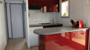 A compact kitchen with a red island, white cabinets, and a window. - semi-detached villa sleeps 6, 3-star furnished holiday accommodation (Saint-Cyprien plage)