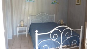 A bedroom with a white metal bed frame, a blue bedspread, two bedside tables with lamps, and a wall-mounted lamp. - Gite on closed wooded grounds (Castelferrus)