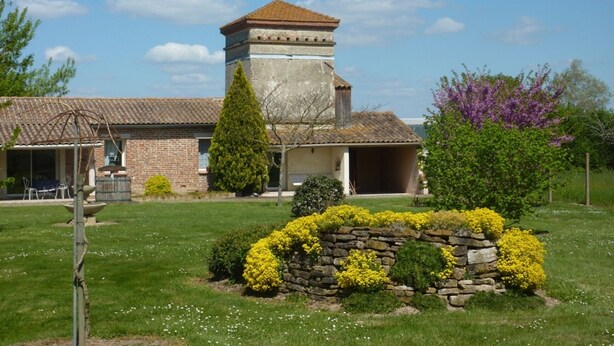 A building with a stone tower, a brick facade, and a garden with yellow flowers and a stone wall. - Gite on closed wooded grounds (Castelferrus)