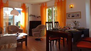 Een eethoek met een tafel voor vier personen, een televisie en oranje gordijnen.