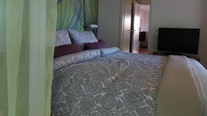 Een slaapkamer met een bed, een televisie en een deur naar een andere kamer.