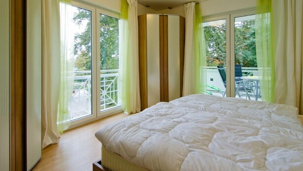 Een slaapkamer met een groot bed, een balkon met een tafel en stoelen en uitzicht op groen.