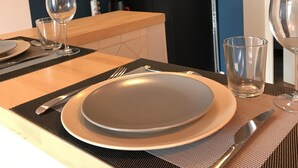 Una mesa de comedor dispuesta con platos, cubiertos y vasos, con un armario negro y una puerta al fondo.
