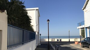 Una calle costera con un edificio blanco, una cerca azul y un coche negro estacionado a la derecha.