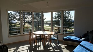A room with a round table and chairs, a sofa, and large windows offering a view of trees and a road.