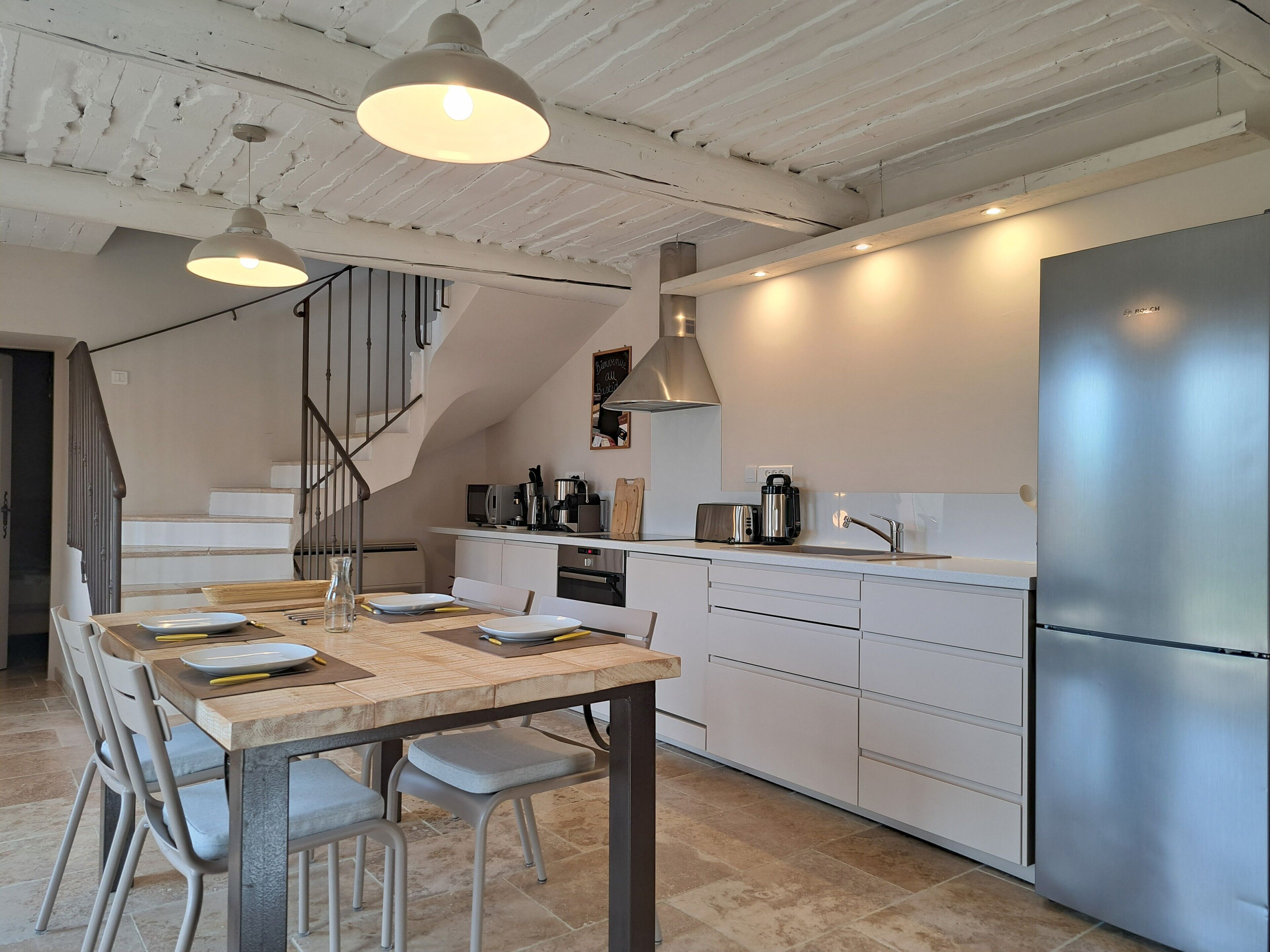 Une cuisine moderne avec un coin repas, des appareils électroménagers en acier inoxydable et un escalier menant à l’étage supérieur.