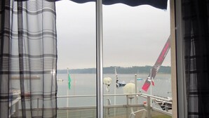 Blick aus einem Fenster auf ein Gewässer, einen Steg und eine Flagge.