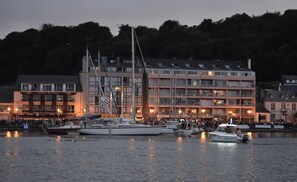 Ein Hotel am Wasser mit mehreren Stockwerken, einer Flagge und Booten im Vordergrund.